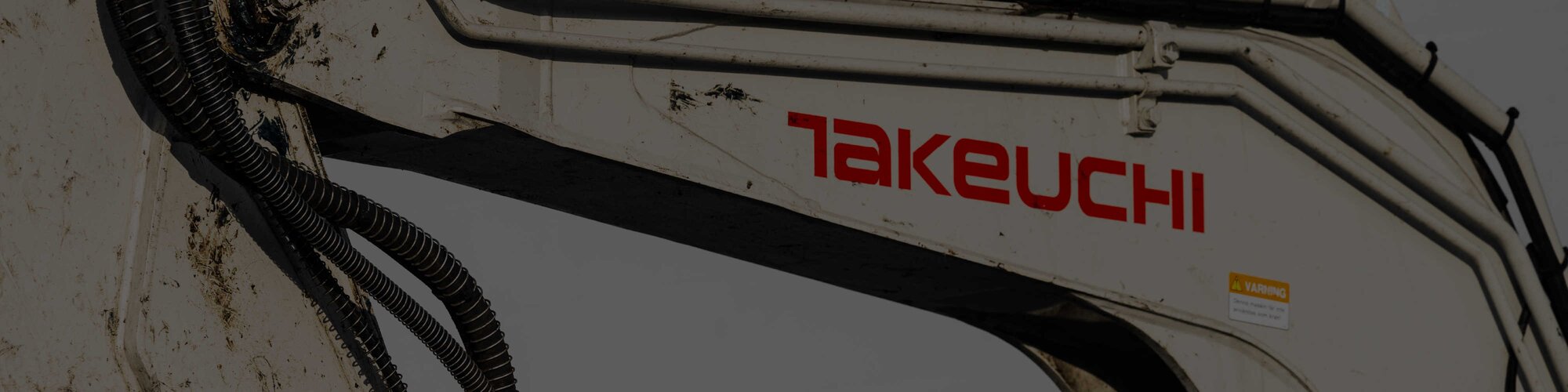 A close-up of the Takeuchi logo on the side of a white compact track loader