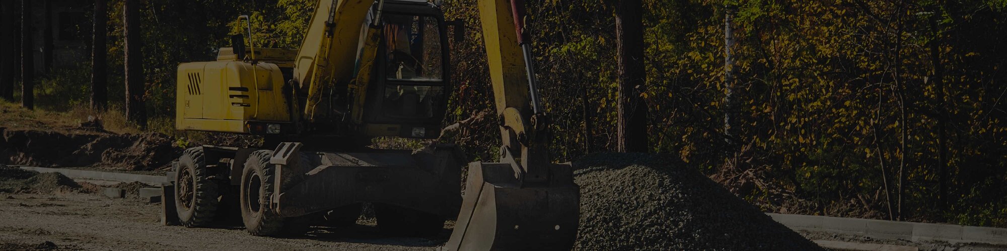 A yellow wheeled excavator with a bucket attachment next to a pile of gravel