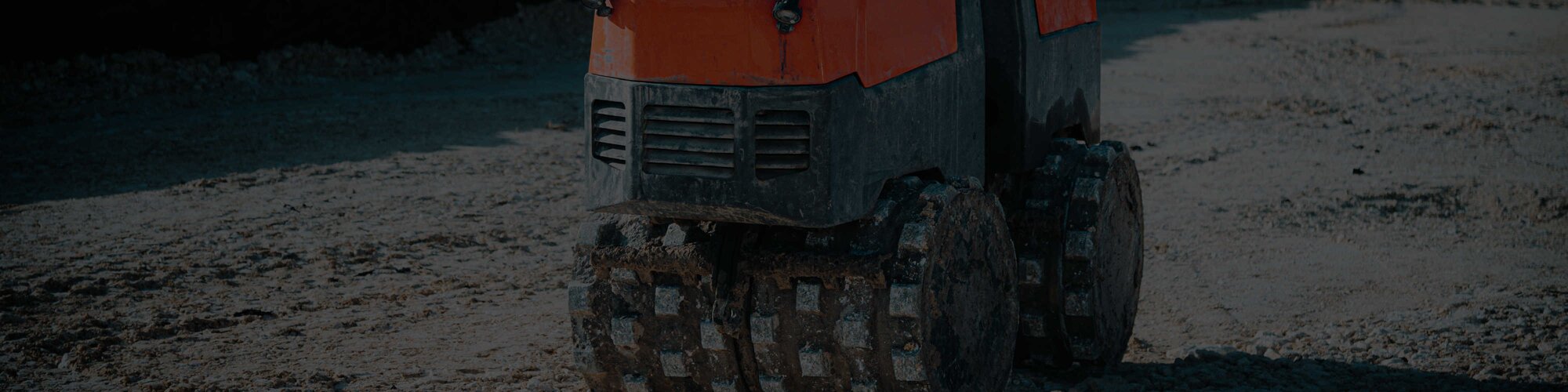 An orange trench roller with sheepsfoot drums moving across dirt.