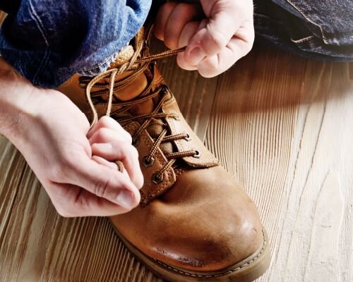 A person tying the laces of a brown work boot