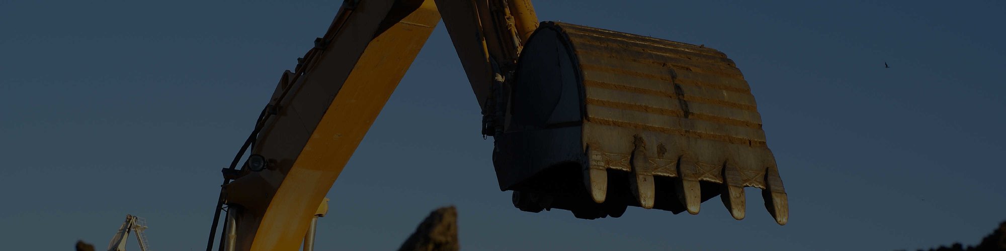 The arm of an excavator with a bucket attachment lifted into the air