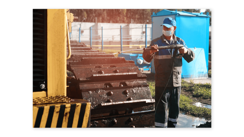 Man using a pressure washer to clean equipment tracks