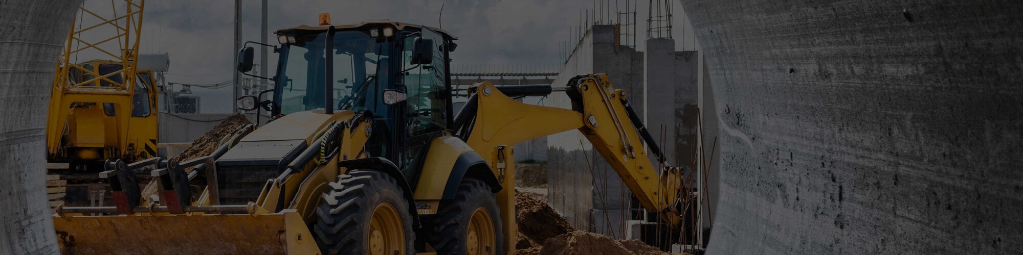 A yellow backhoe working next to a gray wall on a construction site
