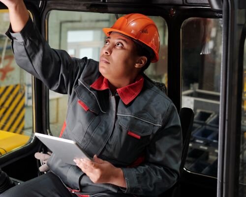 A service technician wearing a work shirt and hard hat, inspecting the operator cab of a machine