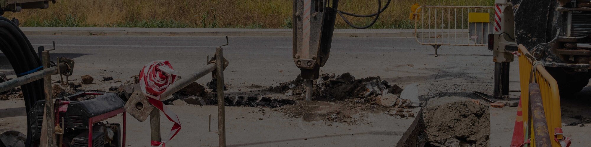 A hydraulic breaker demolishing a roadway with a fence around it