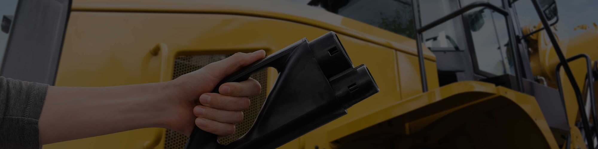 A hand holding a battery charger in front of a yellow machine