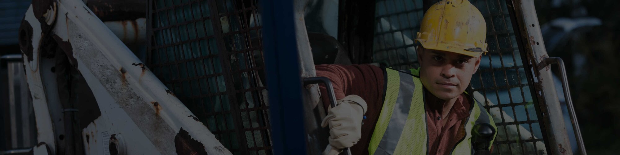An operator exiting the cab of a machine, wearing a hard hat and yellow vest