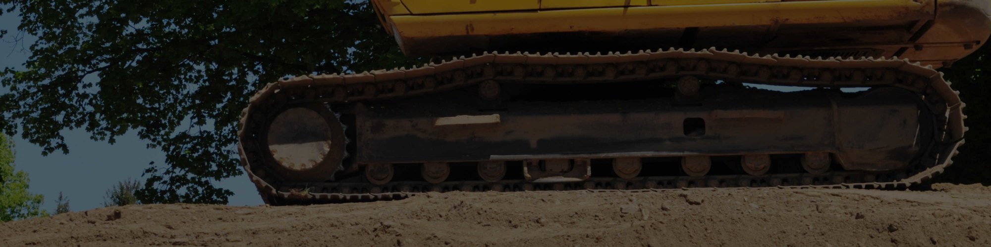 An excavator's tracks sitting on dirt, shown from ground-level 