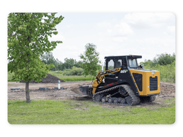 A yellow track loader pushing dirt next to a tree