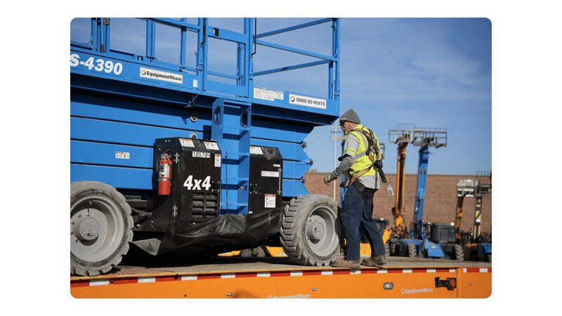 A Genie GS-4390 scissor lift sitting on the top of a trailer with a service technician next to it.