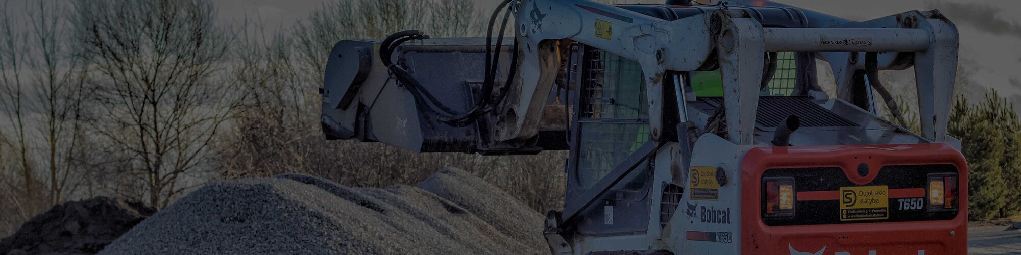 A bobcat compact track loader lifting gravel from a large pile