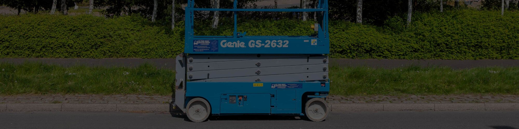 A Genie GS-2632 scissor lift sitting along a curb in front of grass