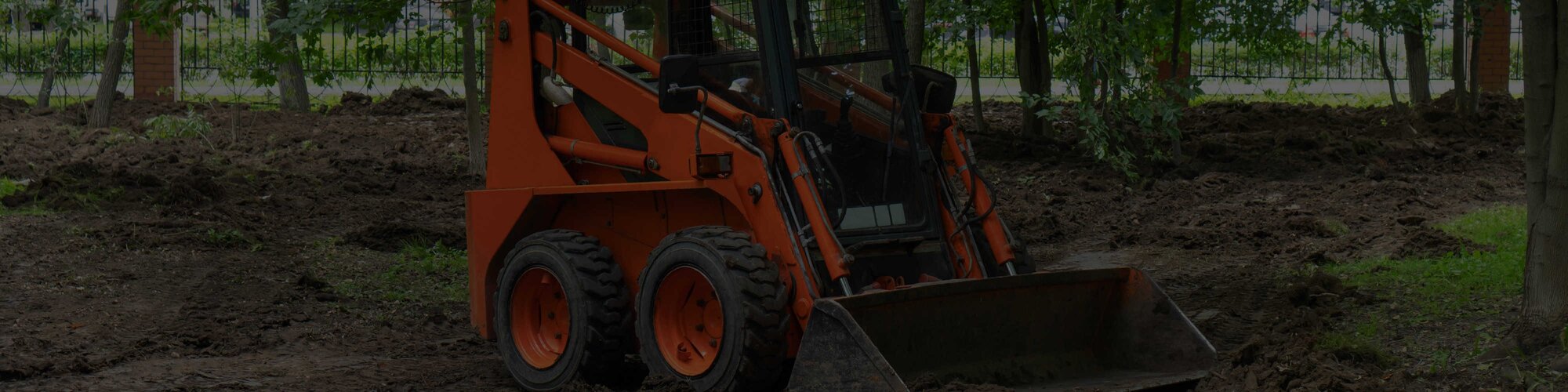 An orange skid steer parked near some trees on a jobsite