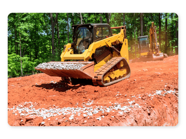 A yellow compact track loader carrying rocks along a dirt path