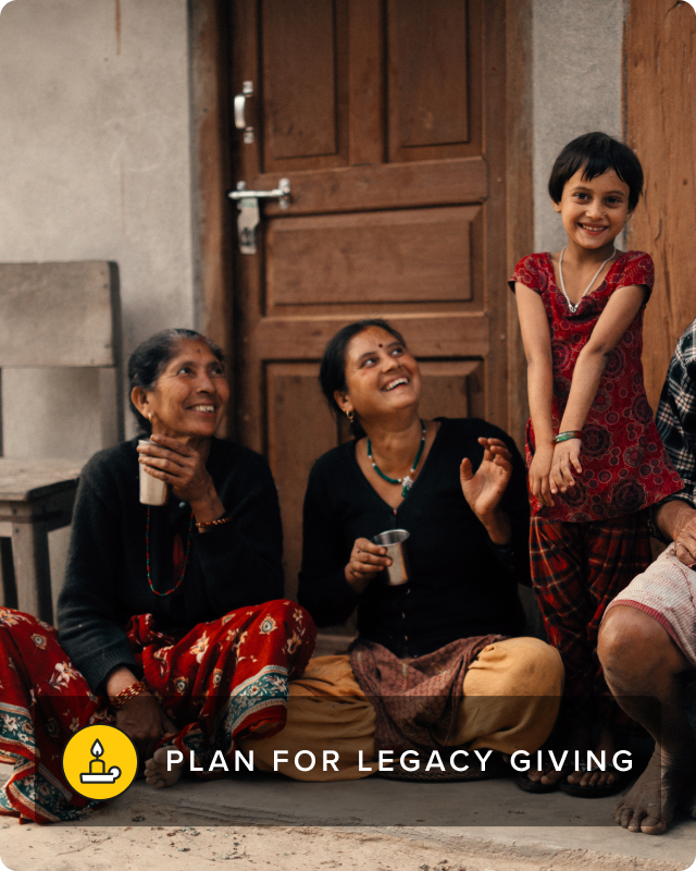 Two women sit smiling towards a young girl who is standing and smiling directly at the camera.