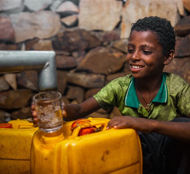 African boy filling a glass of water from a tap