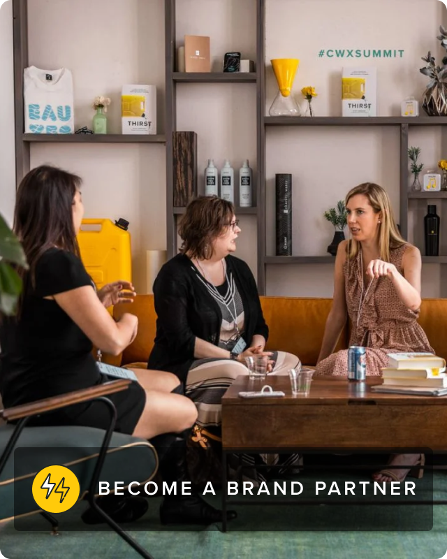 Three woman sit in a living room facing one another in discussion in front of a bookshelf.