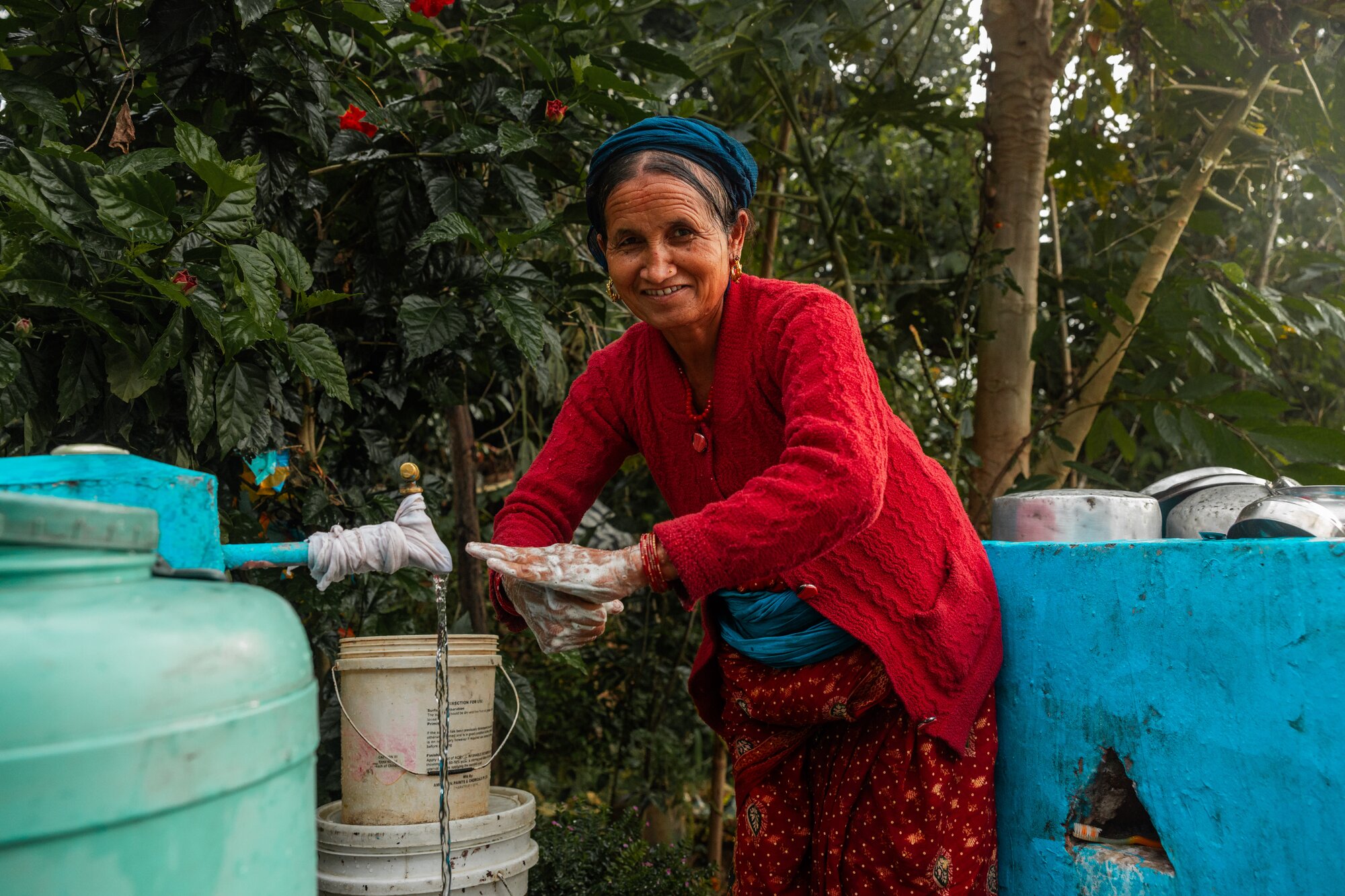 A woman in a red sweater washes her hands at an outdoor water station.