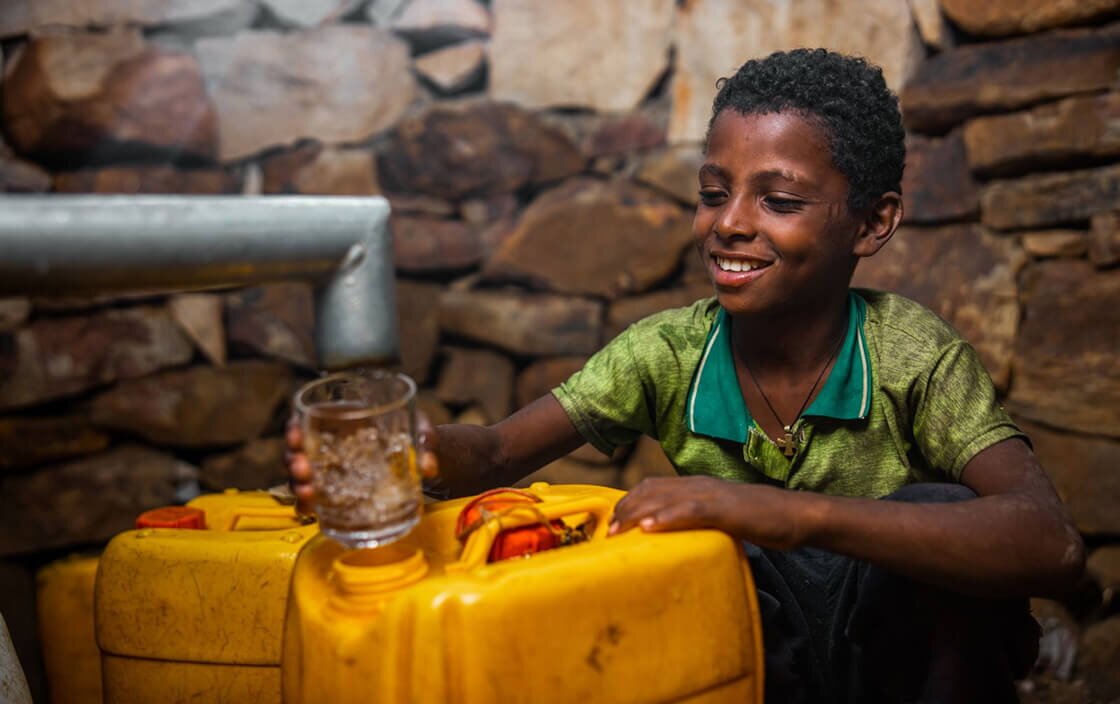 African boy filling a glass of water from a tap
