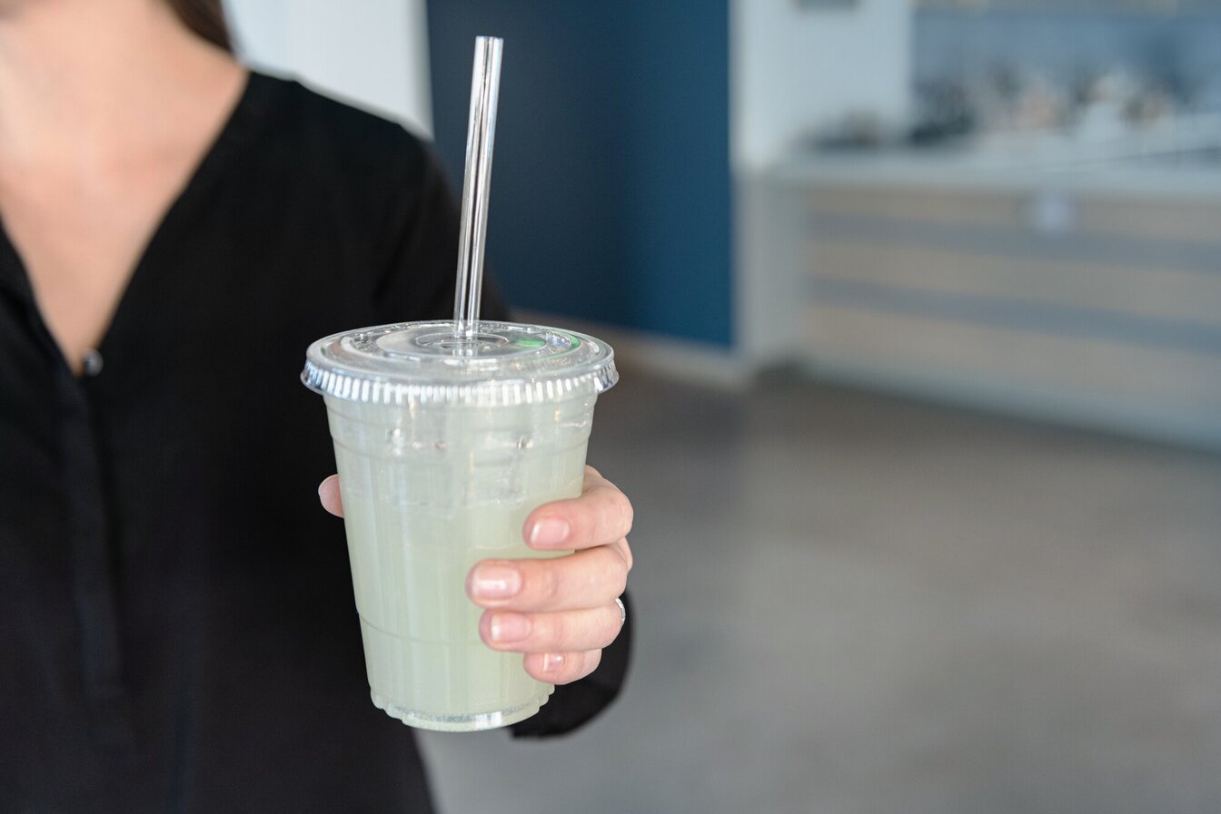 Person holding a cup with a clear compostable drinking straw