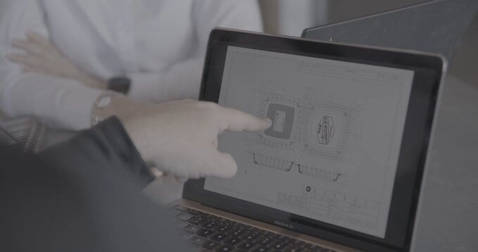 Person pointing at computer screen showing a CAD drawing of a takeout container