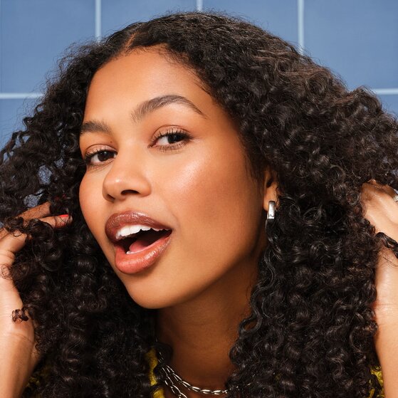 Model with curly hair running fingers through soft, healthy-looking strands after using vegan protein hair care