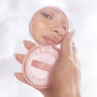 Model Holding Up A Compact Mirror Wearing Cloud Skin Makeup