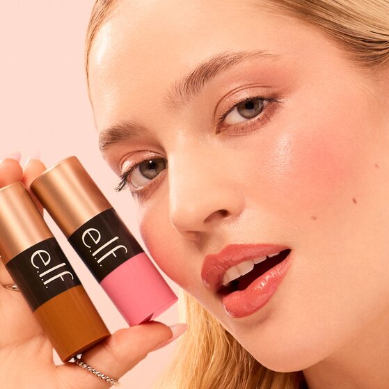 Model holding light pink blush stick and a medium/tan bronzer stick