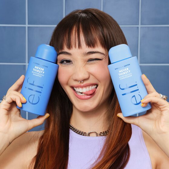 Model holding e.l.f. Never Thirsty Moisturizing Shampoo and Conditioner bottles