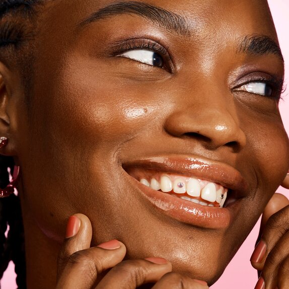 Woman smiling with tooth gems and glowing makeup look
