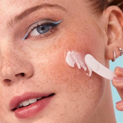 Woman applying makeup cleansing balm with applicator to her cheek
