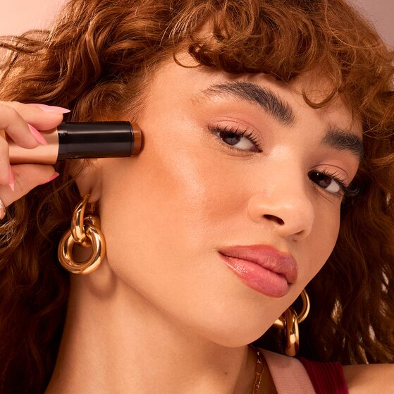 Model applying cream bronzer stick to cheeks