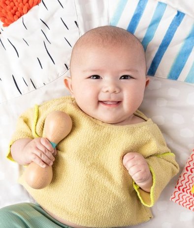 Baby holding Lovevery wooden rattle