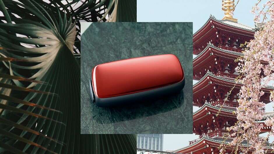 Červený kryt a Ploom zariadenie v pozadí s typickou japonskou stavbou.