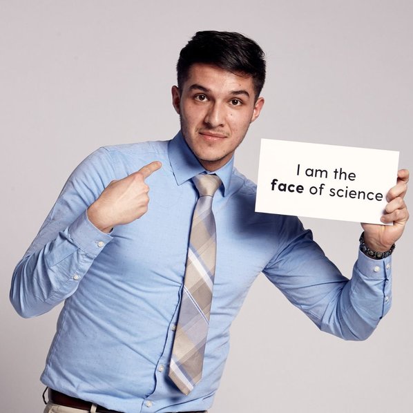 Leonardo Romero-Barajas pointing at his face and holding a sign in his other hand that says "I am the face of science"