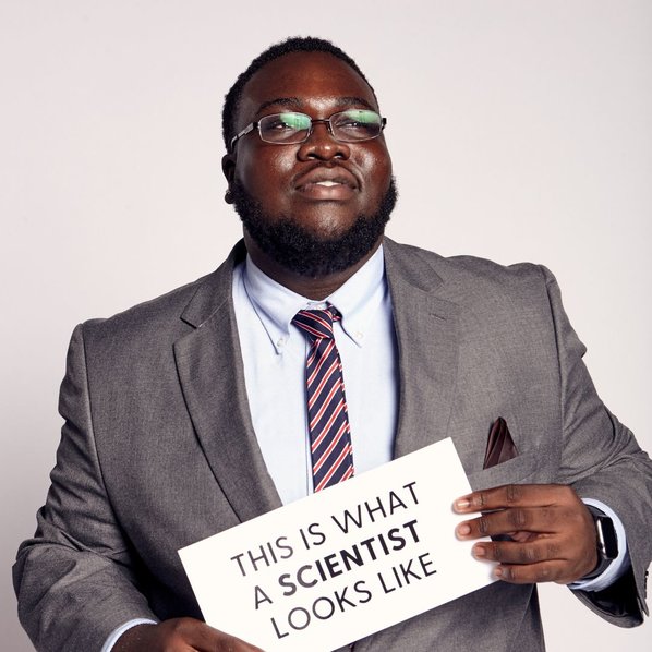 Adetunji Adeniran-Adetoye holding a sign that says "This is what a scientist looks like"
