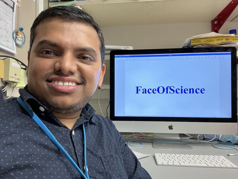 Avik Dutta smiling in front of a computer with FaceOfScience on the screen.