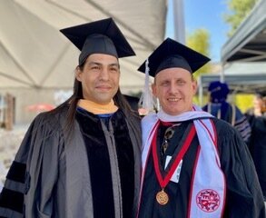 Jose Vargas, PhD, and Zak Peet stand together wearing graduation regalia. 