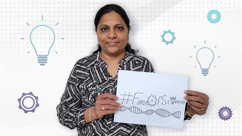 Image of Subhashini Jagu wearing a black and white blouse, standing up holding a white sign that reads "#FacesOfScience"