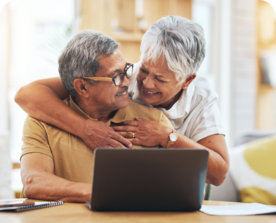 Image of an older couple embracing while looking at a laptop screen.