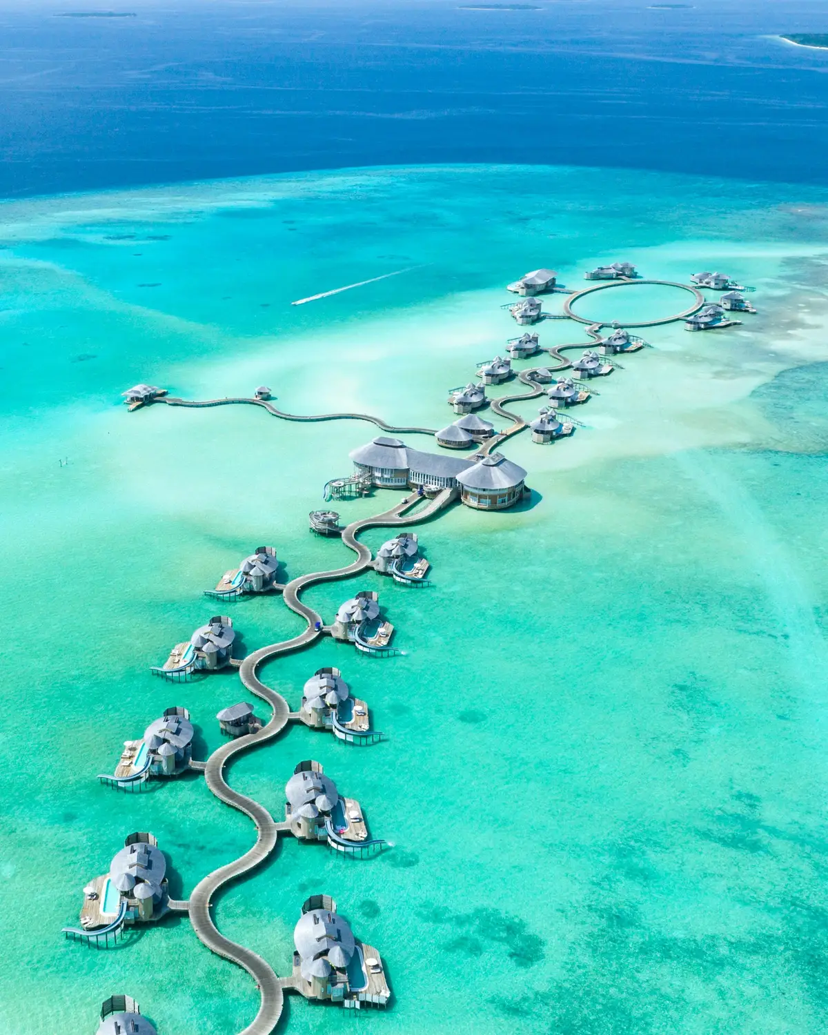 Aerial drone view of luxury overwater villa resort with winding jetty and private pool villas stretching across vast turquoise coral reef lagoon in Maldives
