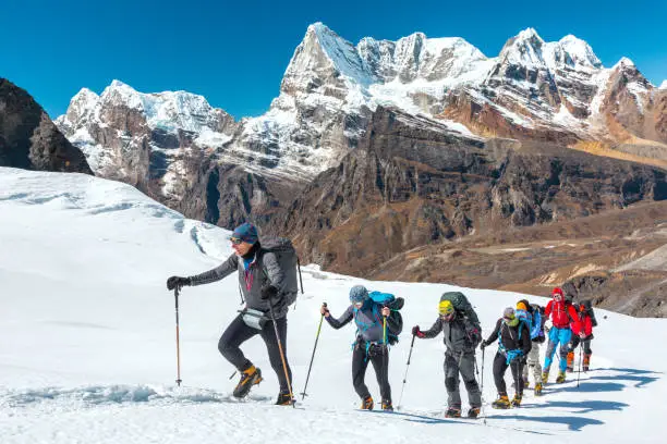 Group of trekkers ascending a snowy slope with rugged Himalayan peaks in the background, Nepal