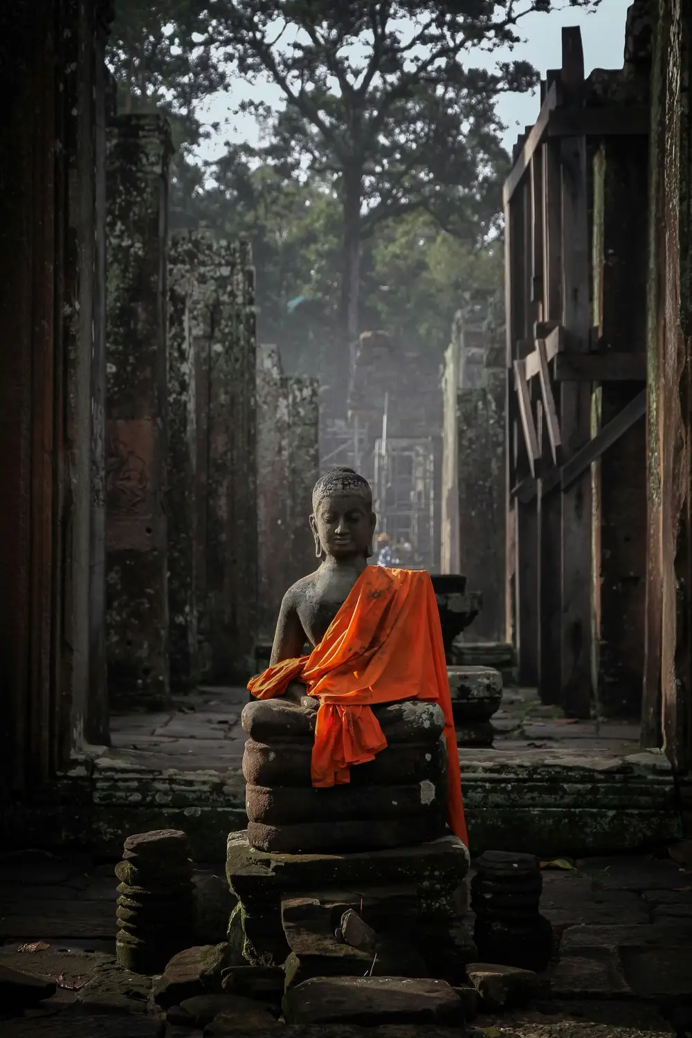 Ancient stone Buddha statue draped in orange saffron robe inside Angkor Wat temple corridor, Siem Reap, Cambodia