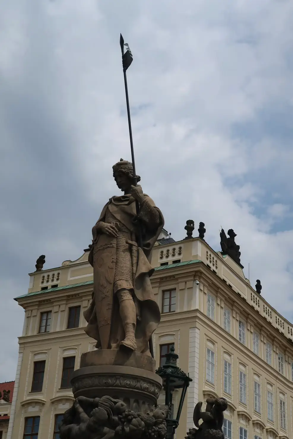 Statue atop a decorative column against a cloudy sky in a Prague square