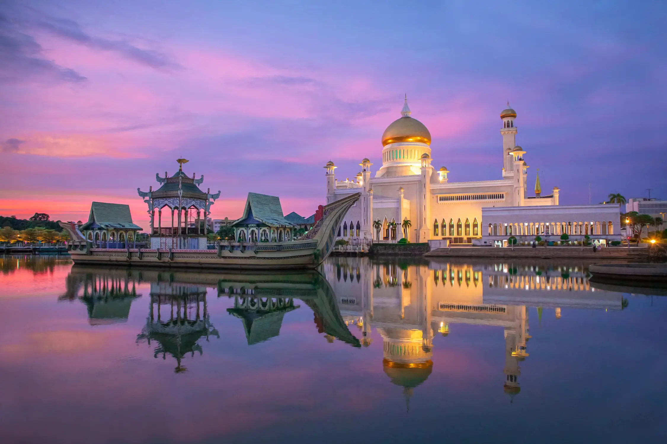 Omar Ali Saifuddien Mosque with golden dome illuminated at twilight, reflecting in still lagoon water with royal barge, Bandar Seri Begawan, Brunei