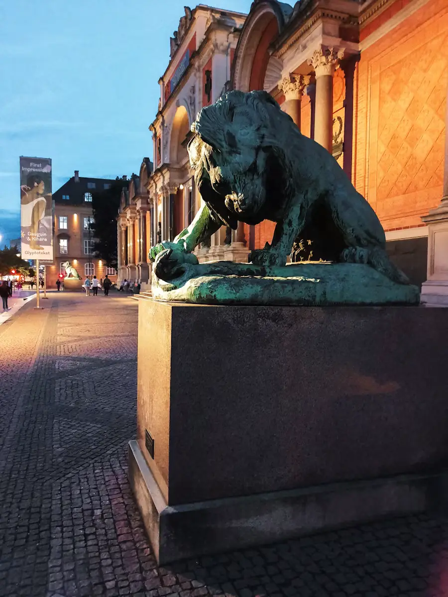 Bronze lion statue on a stone pedestal along a cobblestone street in Denmark at dusk