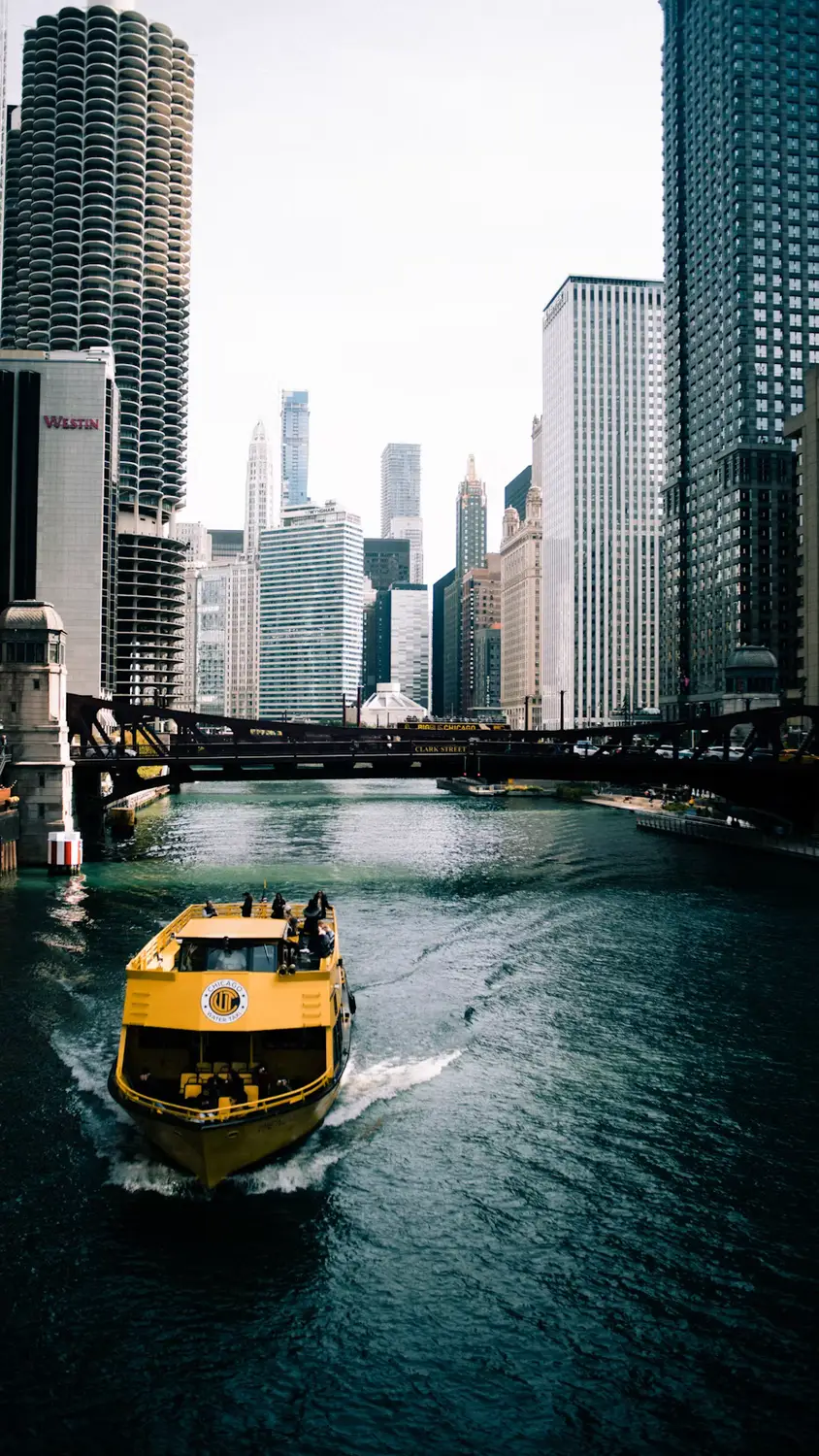 A yellow water taxi cruising along the Chicago River between skyscrapers and under the city's steel bridges.
