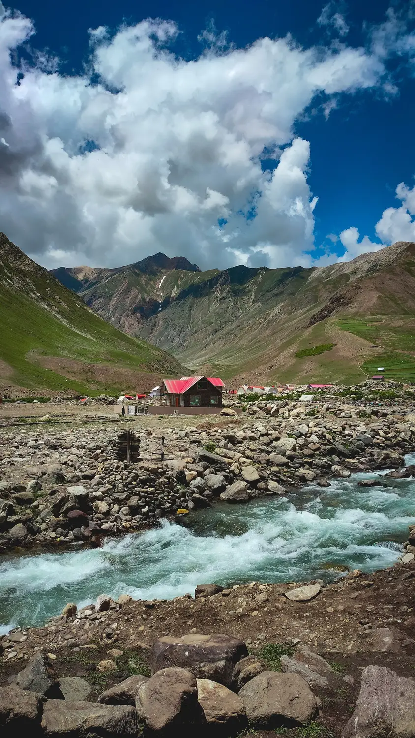 Turquoise glacial river flowing through green mountain valley with red hut Pakistan