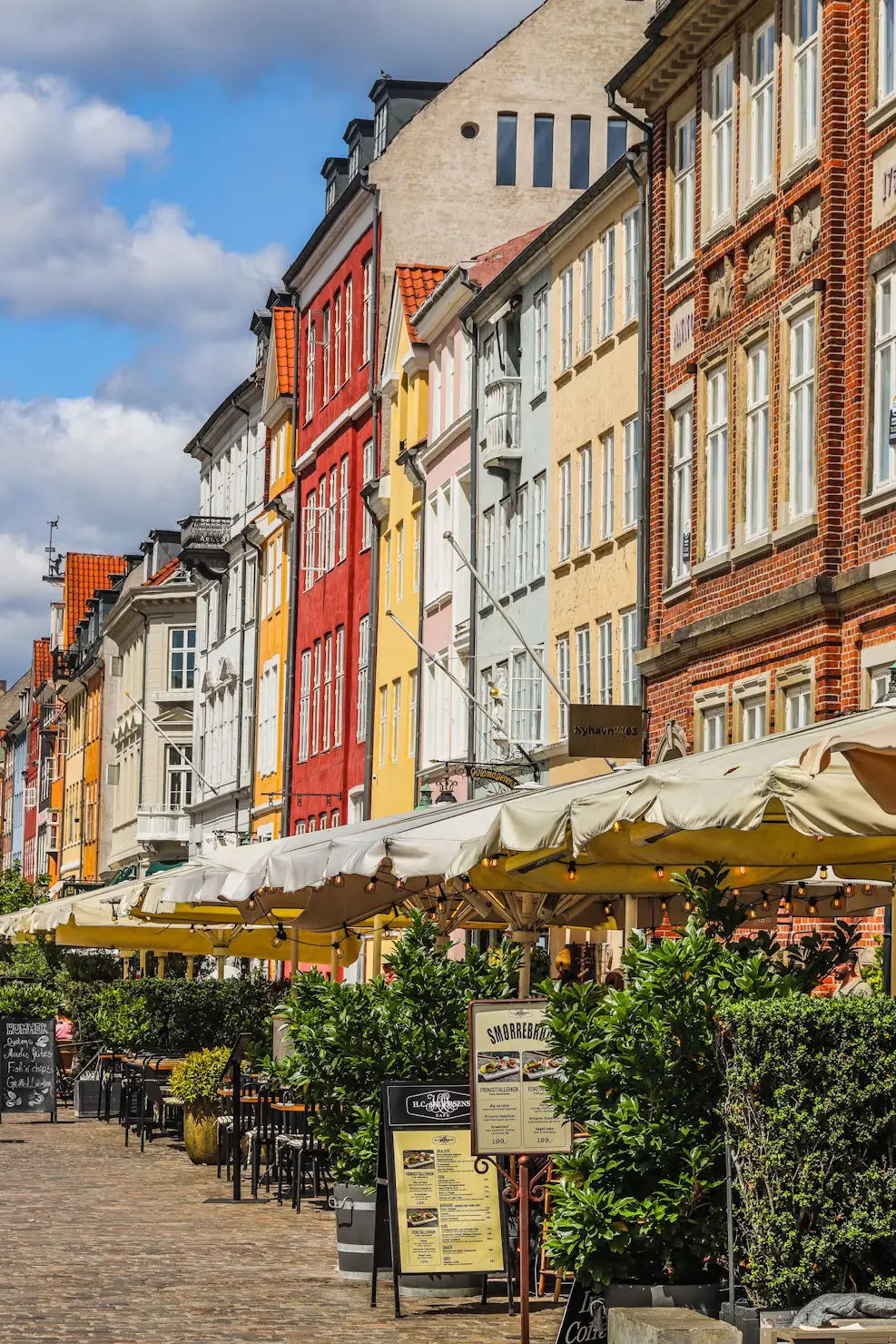 Colorful row houses and outdoor café umbrellas along a bustling Copenhagen street