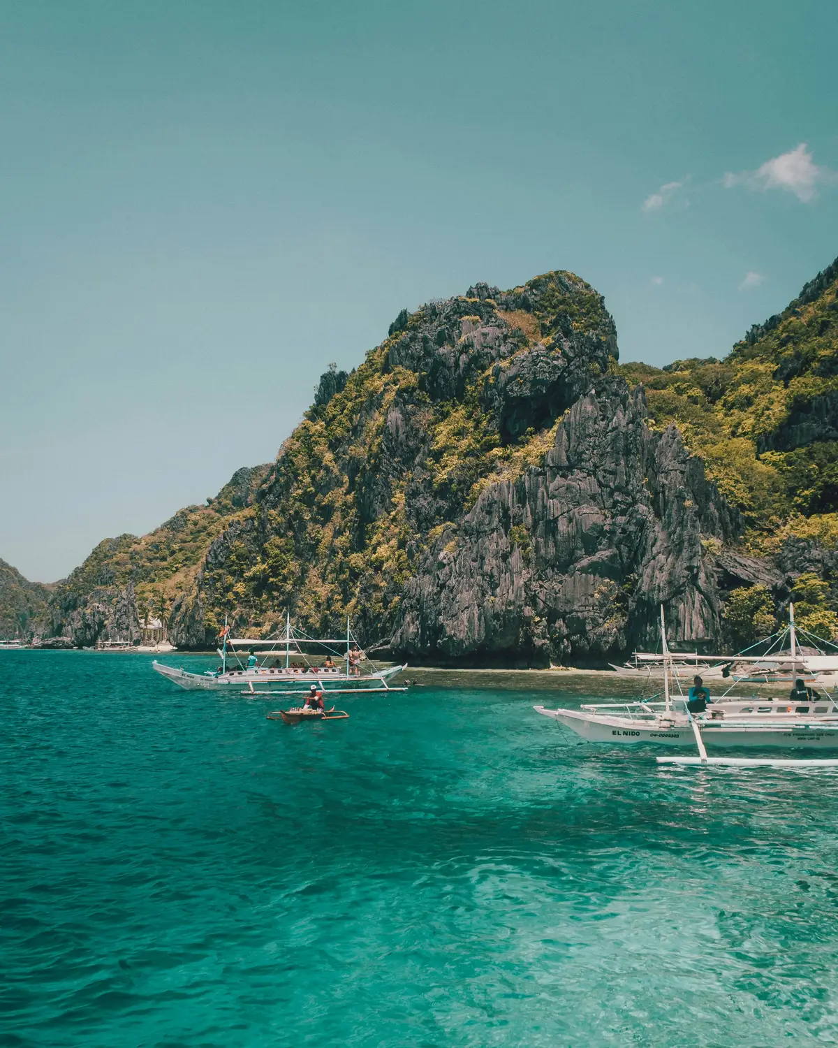 Traditional outrigger boats on turquoise water surrounded by limestone karst islands in El Nido, Palawan, Philippines.